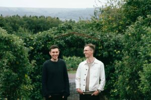 PHOTO OF TWO MEN IN A GARDEN WITH LARGE HEDGES BEHIND THEM.