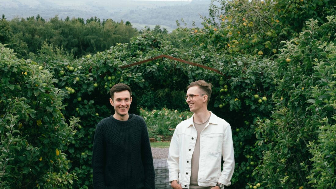 PHOTO OF TWO MEN IN A GARDEN WITH LARGE HEDGES BEHIND THEM.