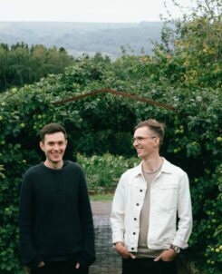 PHOTO OF TWO MEN IN A GARDEN WITH LARGE HEDGES BEHIND THEM.