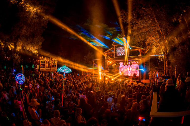 Orange lights shooting out from a wooden stage structure with a packed crowd