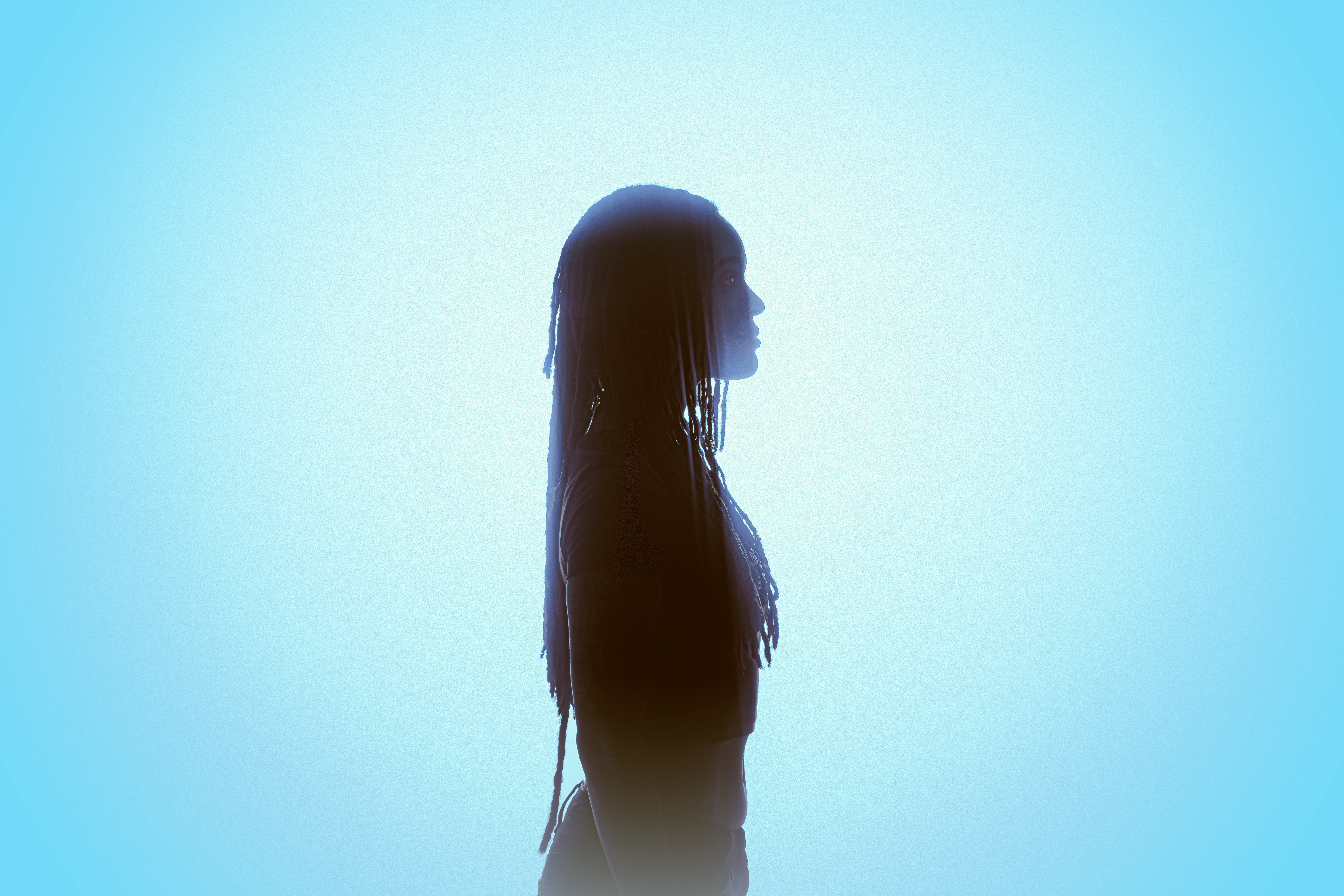 A Hundred Drums press photo. Side shot, standing in front of bright blue background