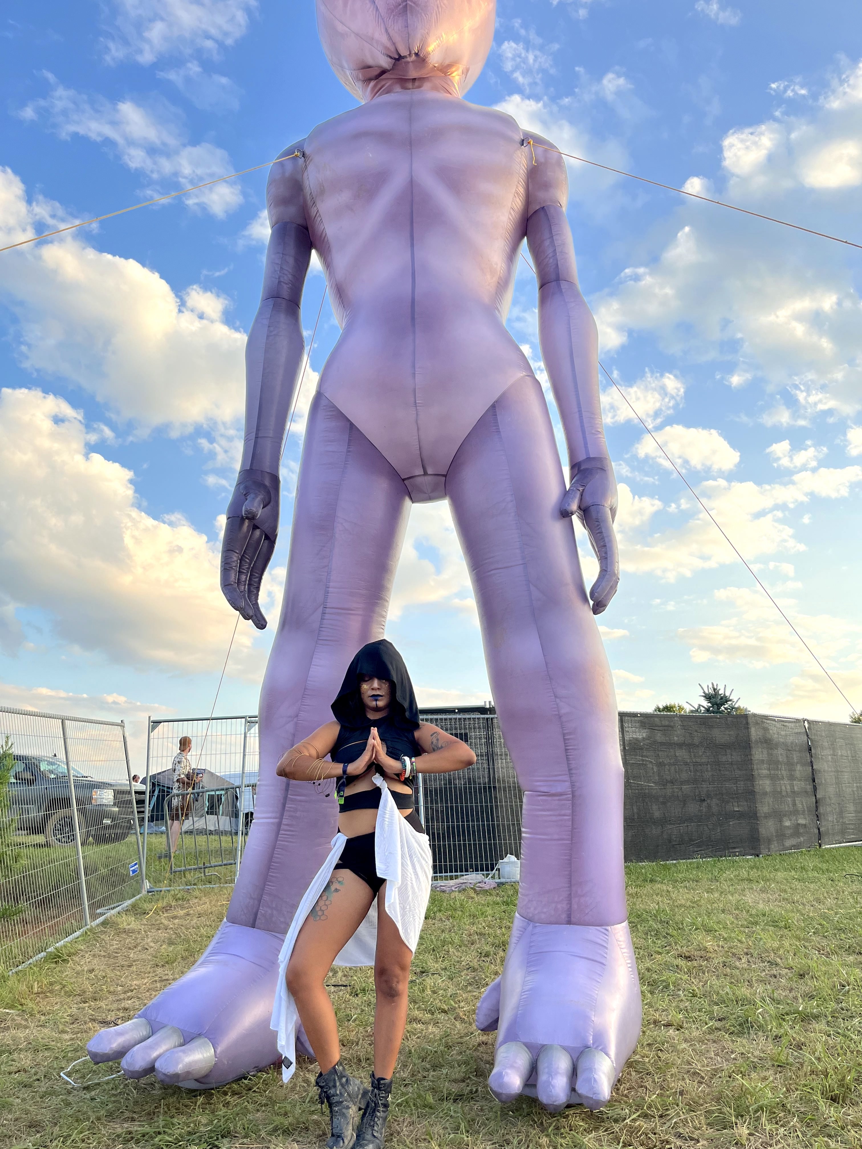 Festival fashion 2023: women wearing black hood white half-skirt in front of large purple inflatable.