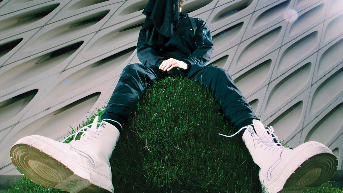 Modapit press photo: sitting on grass hill with face covered.