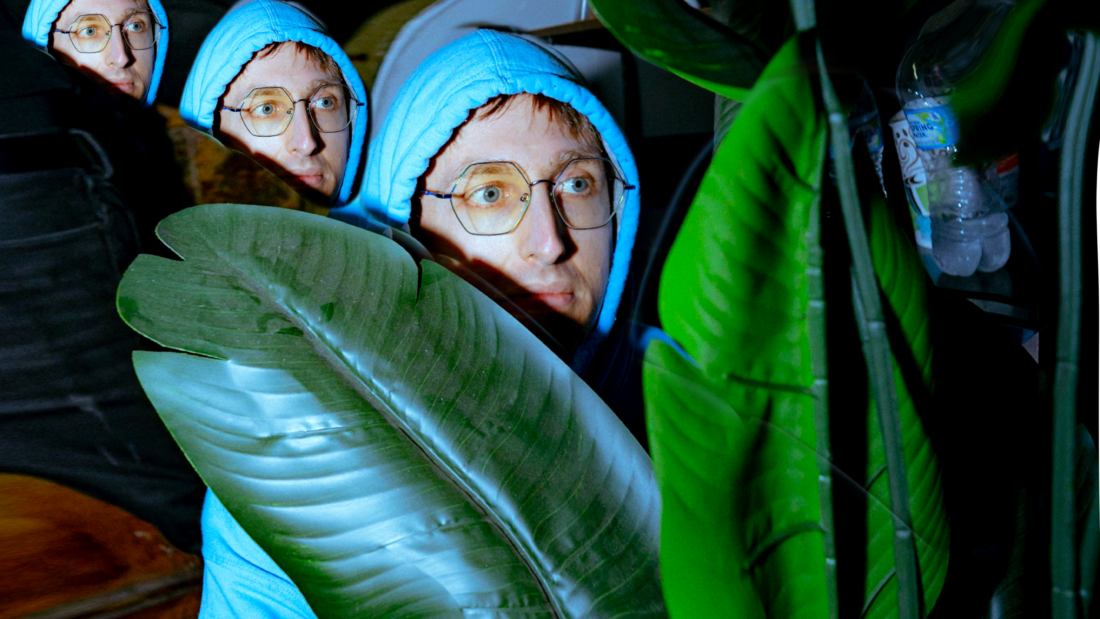 Yheti press shot. Man in blue hoodie peeking over a big plant leaf