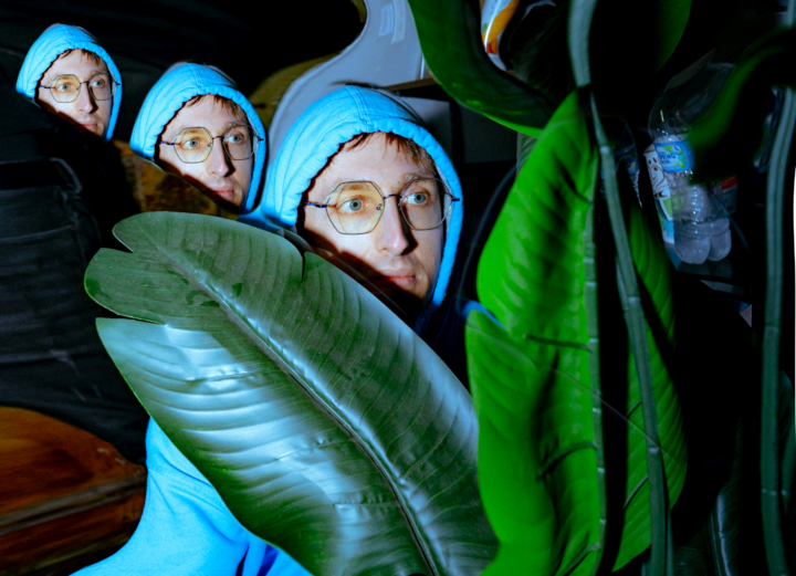 Yheti press shot. Man in blue hoodie peeking over a big plant leaf