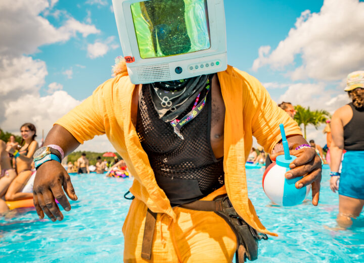 Man with a TV head and orange jacket dancing in a pool at Imagine Music Festival 2023