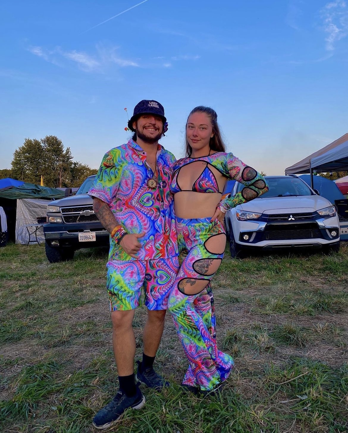 A man and a woman dressed in 70s psychedelic disco outfits posing at their camp site during Lost Lands 2023