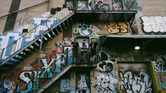 Ternion Sound trio standing outside on staircase covered in graffiti