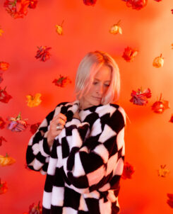 Maddy O'Neal wearing a checkered jacket in front of an orange screen