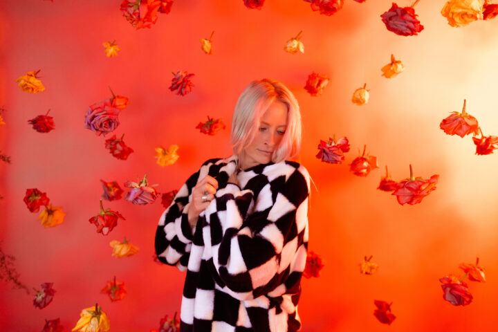 Maddy O'Neal wearing a checkered jacket in front of an orange screen
