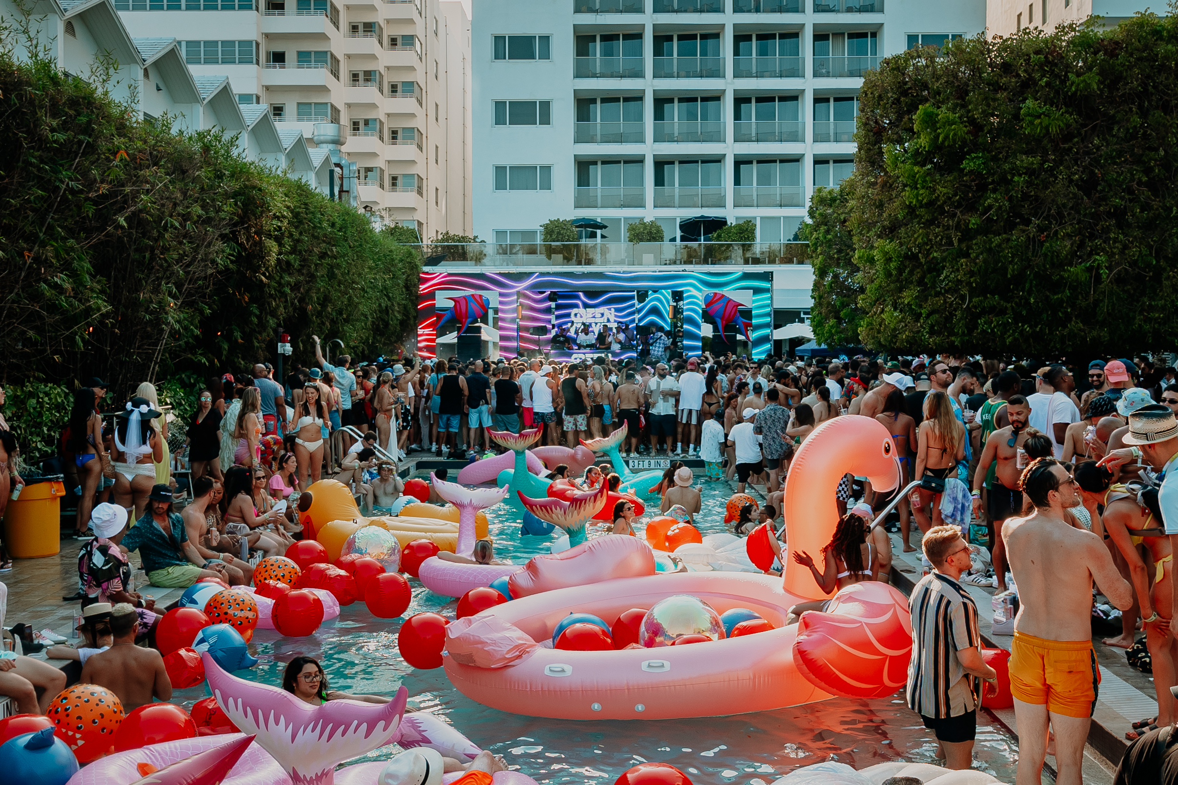 Pool party in Miami. People swimming while a DJ plays poolside.