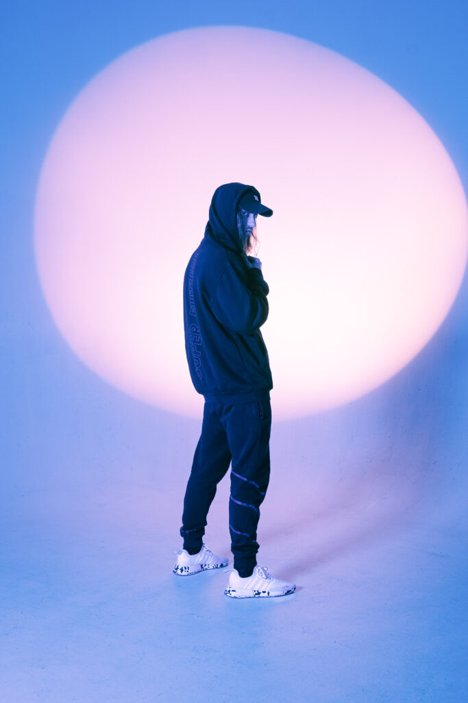 Super future DJ posing in a hoodie in front of a purple wall.