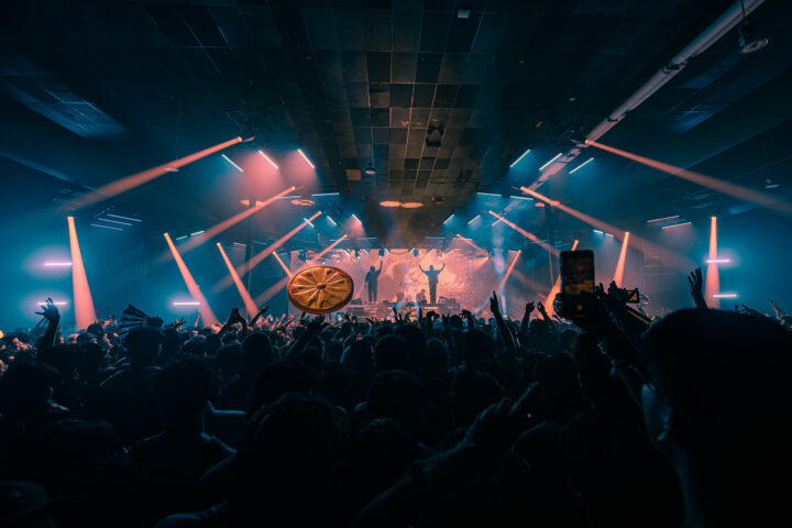 Two DJs standing on stage with strobe lights and an LED screen behind them