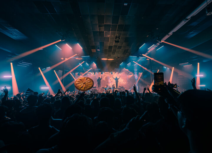 Two DJs standing on stage with strobe lights and an LED screen behind them