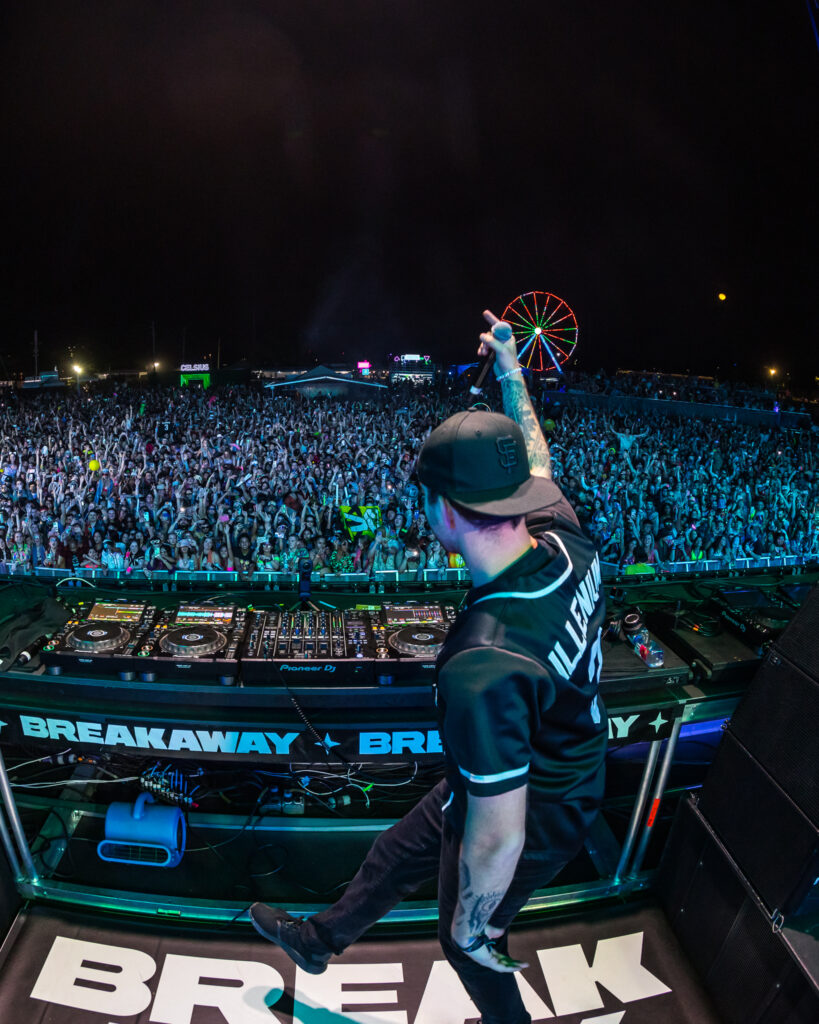 DJ ILLENIUM playing at BREAKAWAY festival in front of a massive crowd with blue lights and a ferris wheel in the background