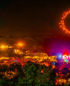 Texas Eclipse Festival. Drones forming a red circle in the sky while a crowd gathers around a massive stage, surrounded by hills and trees.