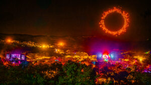 Texas Eclipse Festival. Drones forming a red circle in the sky while a crowd gathers around a massive stage, surrounded by hills and trees.