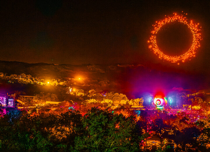 Texas Eclipse Festival. Drones forming a red circle in the sky while a crowd gathers around a massive stage, surrounded by hills and trees.