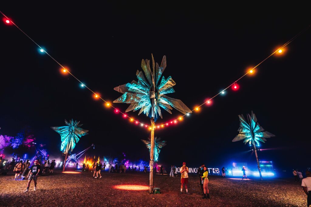 Lightning in a Bottle 2024 venue after dark, with sculptures of palm trees and colorful lights.