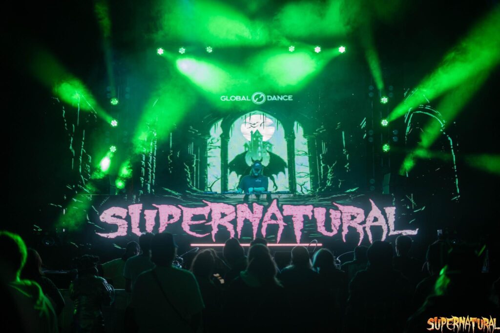 Dj standing behind the decks in front of a "SUPERNATURAL sign for the Supernatural festival