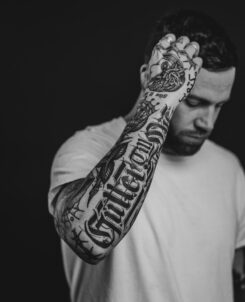 Jansten posing in front of black background. Full arm sleeve tattoo. Black and white.