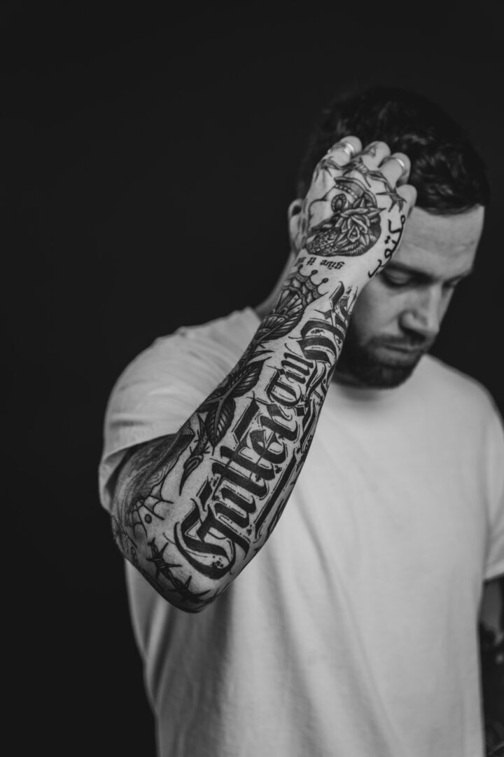 Jansten posing in front of black background. Full arm sleeve tattoo. Black and white.