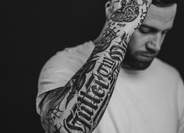 Jansten posing in front of black background. Full arm sleeve tattoo. Black and white.