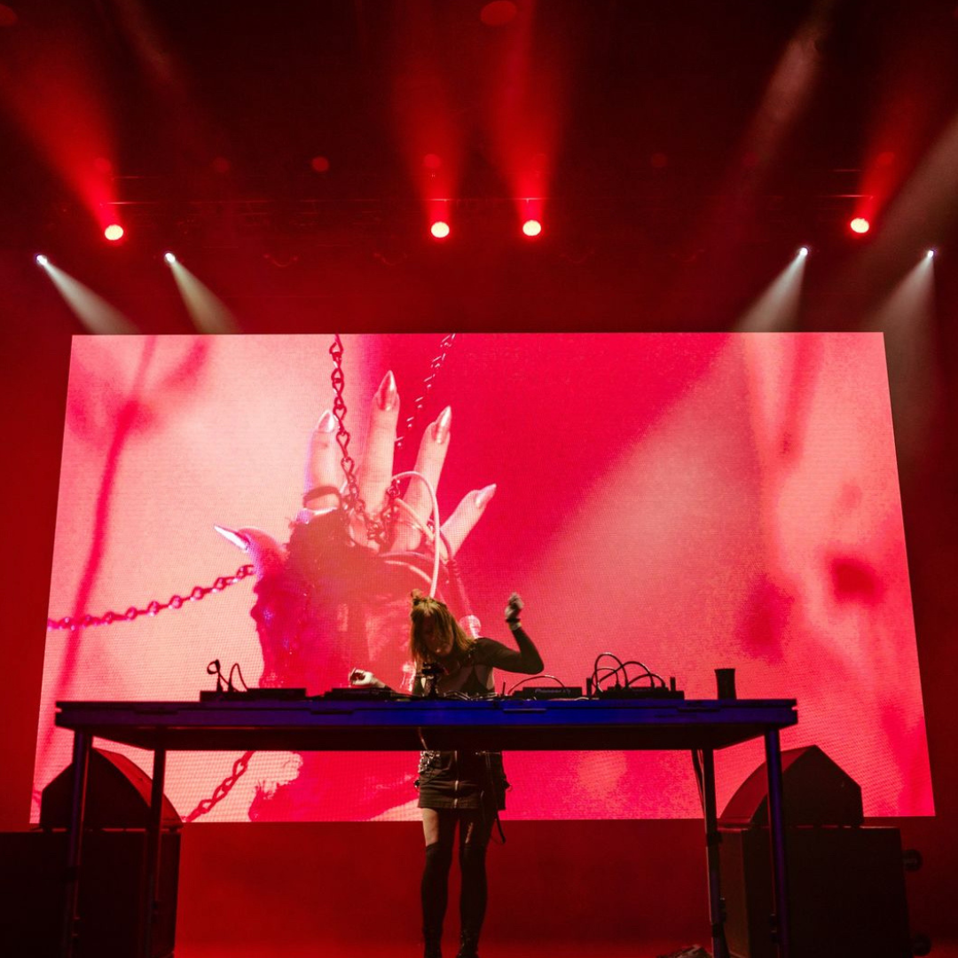 Dj playing in front of a red screen on stage.