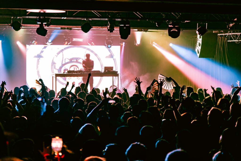 Jantsen playing a DJ set on stage in front of a big crowd. Indoor venue. Pink and blue lights.