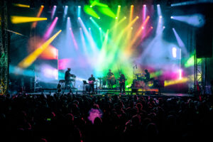 Bright colorful lights on a massive stage while jam band plays to large crowd