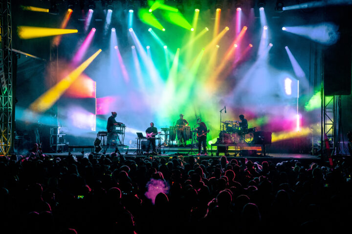 Bright colorful lights on a massive stage while jam band plays to large crowd