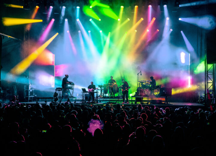 Bright colorful lights on a massive stage while jam band plays to large crowd